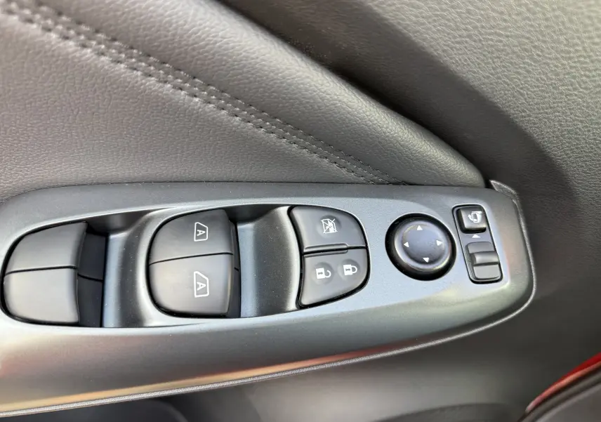 Gros plan sur les commandes de lève-vitres et rétroviseurs côté conducteur du Nissan Juke rouge Fuji 2025.