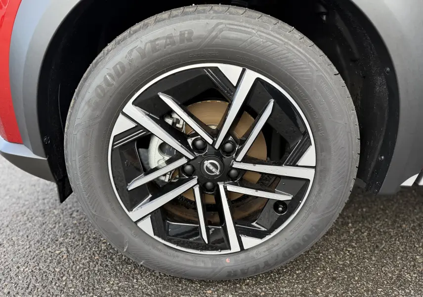 Gros plan sur la roue avant gauche du Nissan Juke rouge Fuji, mettant en valeur la jante noire et argentée au design moderne.