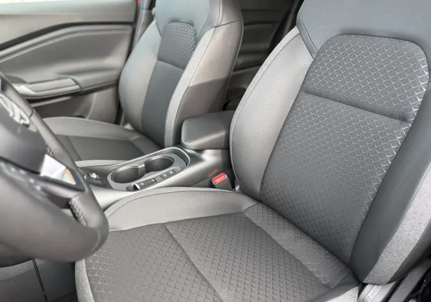 Vue rapprochée des sièges avant noirs et gris du Nissan Juke 2025, mettant en valeur la texture et l'accoudoir central.