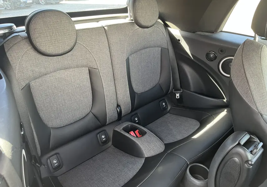 Vue intérieure arrière de la MINI Cabriolet F57 avec sellerie tissu/cuir gris et noir, appuie-têtes ronds et ceintures visibles.