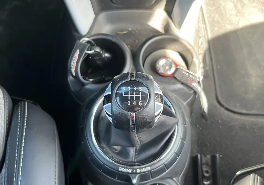 Gros plan sur le levier de vitesse manuel de la MINI Cabriolet bleu, avec clé et porte-clés John Cooper Works à proximité.