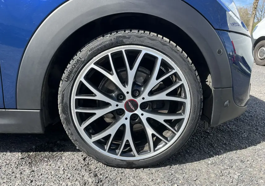 Gros plan sur la roue avant droite d'une MINI Cabriolet F57 Cooper S bleu, avec jante alliage multibranches et logo John Cooper Works.