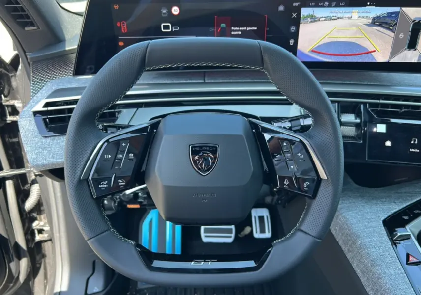 Vue centrée sur le volant cuir multifonctions du Peugeot 3008 New Hybrid GT avec écran digital et affichage caméra 360° en arrière-plan.