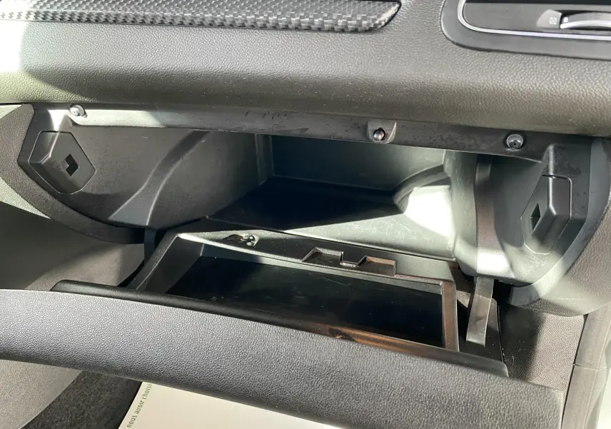 Gros plan sur la boîte à gants ouverte de la Renault Mégane IV Berline gris, montrant l'intérieur en plastique noir.