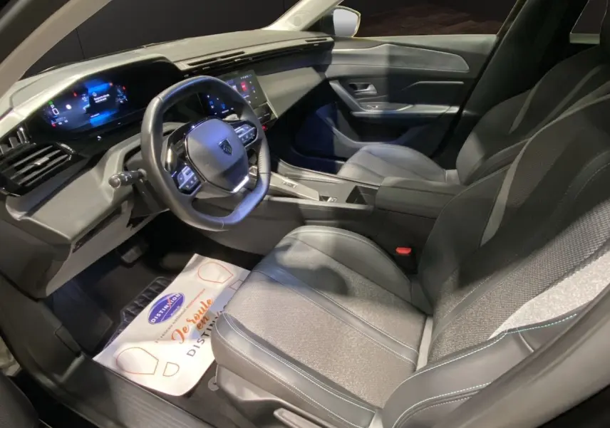Intérieur noir de la Peugeot 308 2024, vue côté conducteur montrant le tableau de bord numérique et les sièges en tissu et cuir.