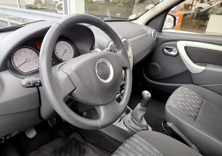 Vue intérieure côté conducteur de la Dacia Sandero 2011, volant cuir noir et tableau de bord gris clair.