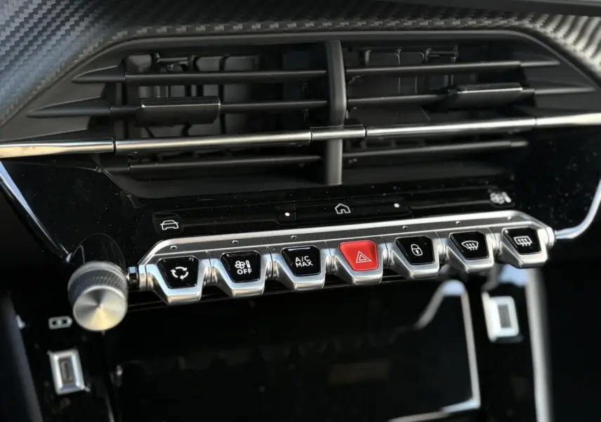 Gros plan sur la console centrale du Peugeot 2008 Hybrid 145 e-DSC6 Allure 2025, boutons argentés et rouge, finition noire brillante.