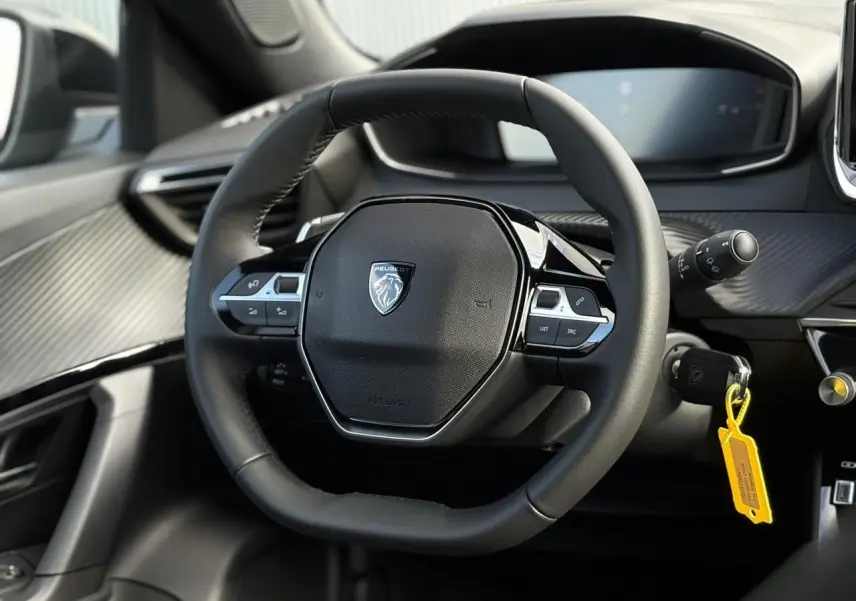 Vue rapprochée du volant compact en cuir noir du Peugeot 2008 Hybrid 145 e-DSC6 Allure avec tableau de bord numérique.