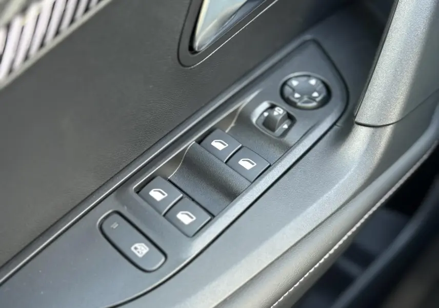 Gros plan sur les commandes des lève-vitres et réglages des rétroviseurs côté conducteur du Peugeot 2008 Hybrid 145 gris Artense.