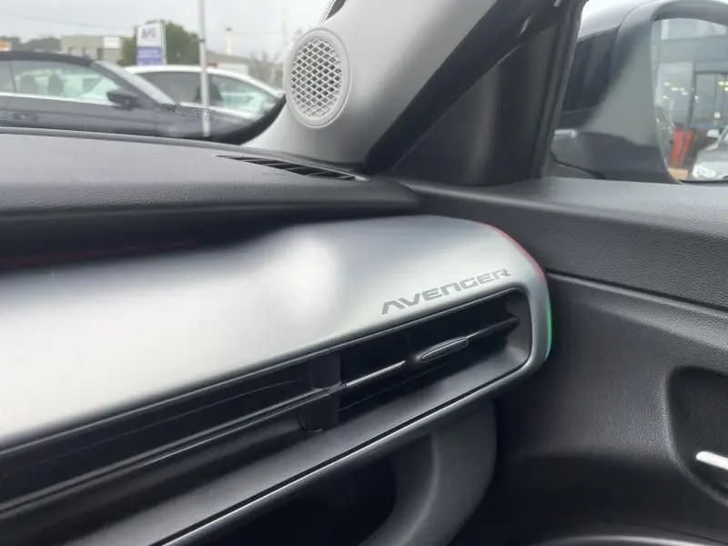 Détail intérieur côté passager du tableau de bord gris métal avec inscription Avenger et haut-parleur rond.