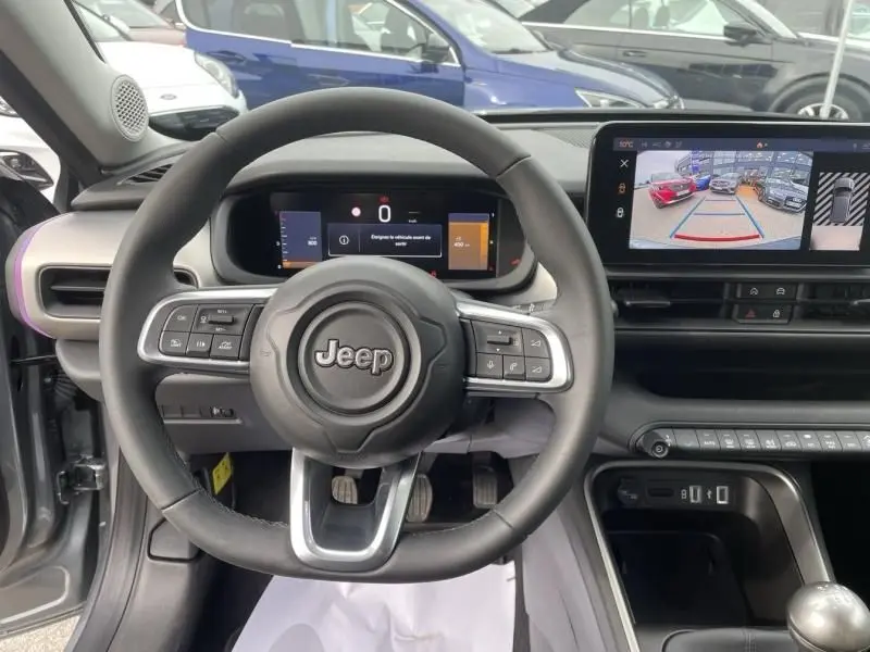 Vue intérieure centrée sur le volant Jeep d’un Avenger gris métal 2025 avec écran numérique et caméra de recul affichée.