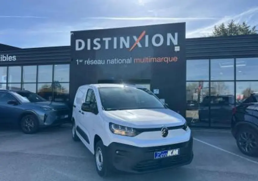 Vue 3/4 avant d'un utilitaire Citroën Berlingo blanc Icy avec pare-chocs noir devant un bâtiment Distinxion.