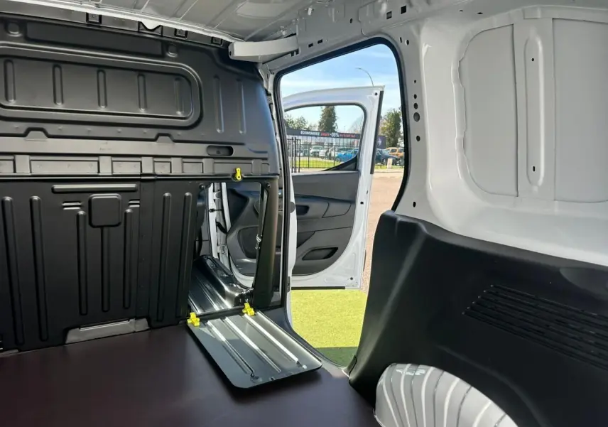 Vue intérieure arrière du Citroën Berlingo blanc Icy, porte latérale droite ouverte et cloison cabine partiellement rabattue.