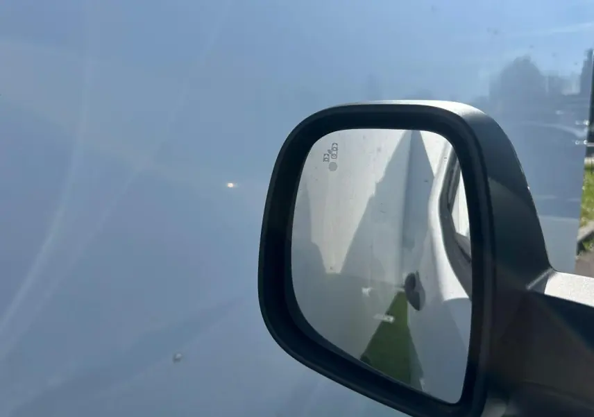 Rétroviseur droit noir brillant du Citroën Berlingo blanc Icy, vue rapprochée sur fond de carrosserie blanche.