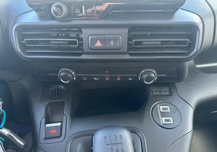 Vue rapprochée du tableau de bord et console centrale noire du Citroën Berlingo blanc, avec boîte manuelle et commandes climatisation.