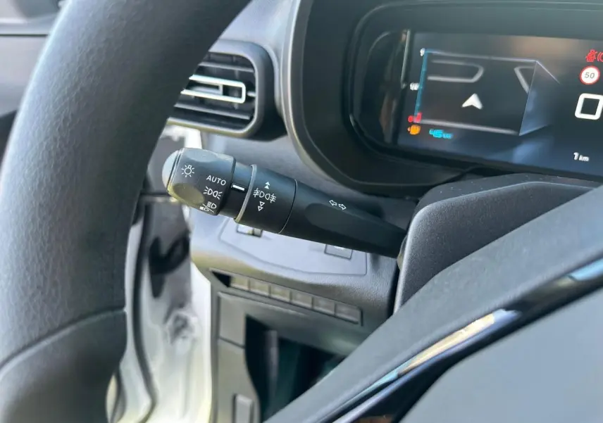 Vue rapprochée du combiné numérique 10'' et du commodo d'éclairage du Citroën Berlingo blanc, côté conducteur.