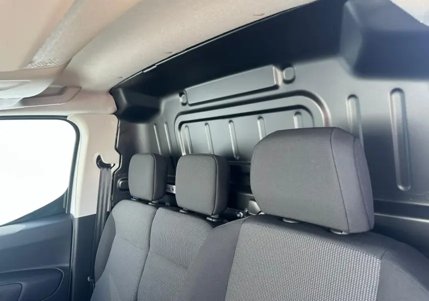 Vue intérieure côté droit du Citroën Berlingo blanc, montrant les sièges avant en tissu gris et cloison métallique arrière.
