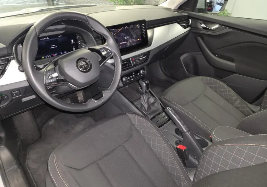 Vue intérieure côté conducteur du Skoda Kamiq 2023, montrant le volant cuir, tableau de bord digital et sièges tissu noirs.