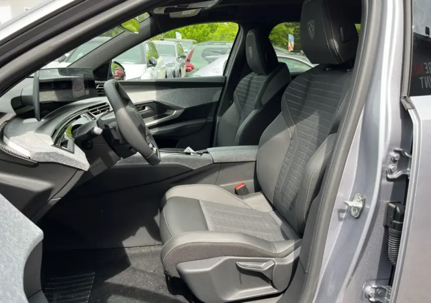 Intérieur avant droit du Peugeot 3008 New Hybrid 145 GT 360 2025, sièges en cuir gris avec logo Peugeot brodé.