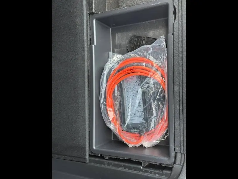 Gros plan sur le câble de recharge orange dans le compartiment de rangement du coffre du Peugeot 3008 Hybride Rechargeable noir.