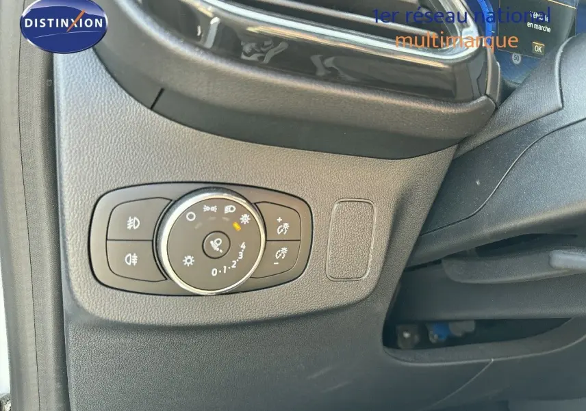 Gros plan sur le bouton de réglage des phares à gauche du volant dans l'habitacle du Ford Puma blanc 2022.