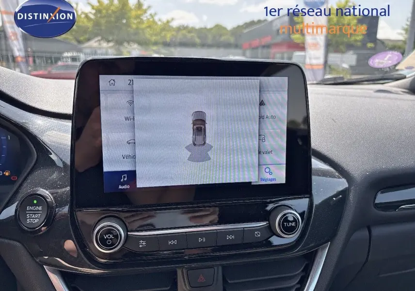 Vue intérieure centrée sur l'écran tactile du tableau de bord d'une Ford Puma blanche, affichant l'aide au stationnement.