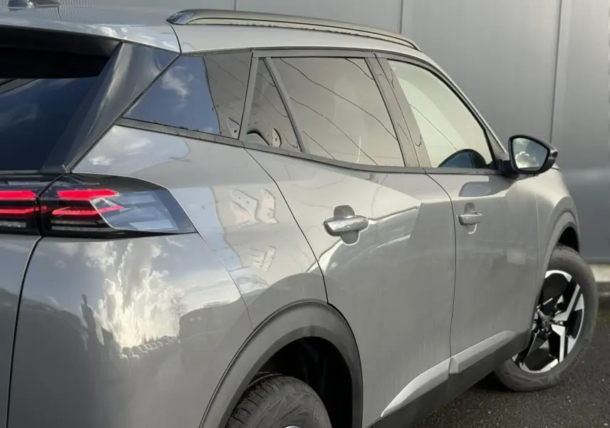 Peugeot 2008 Hybrid 145 e-DSC6 Allure gris Selenium, vue 3/4 arrière droit avec jantes alliage bi-ton et barres de toit noires.