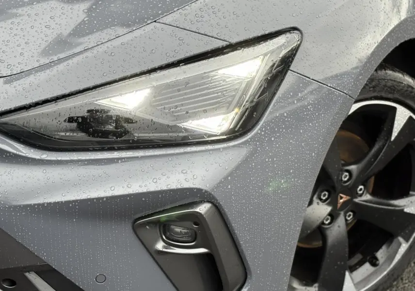 Gros plan sur l'avant droit gris Graphene d'une CUPRA LEON ST 2025, avec phare LED allumé et jante alliage noire.