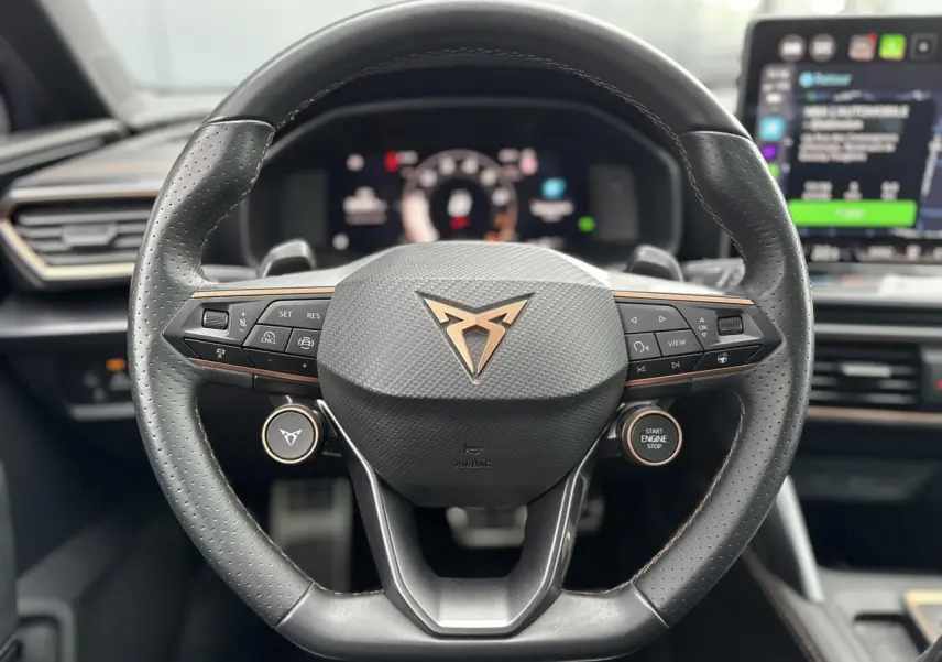 Gros plan sur le volant cuir perforé noir avec logo CUPRA cuivré et commandes multifonctions du CUPRA LEON ST 2025.