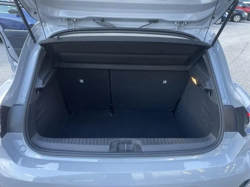 Coffre ouvert vu de l'arrière d'une Renault Clio V gris métal 2025, montrant l'espace de chargement vide et l'éclairage intérieur.