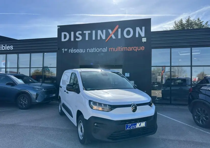 Vue 3/4 avant droite du Citroën Berlingo blanc Icy avec calandre noire et jantes tôle grises, devant un bâtiment Distinxion.