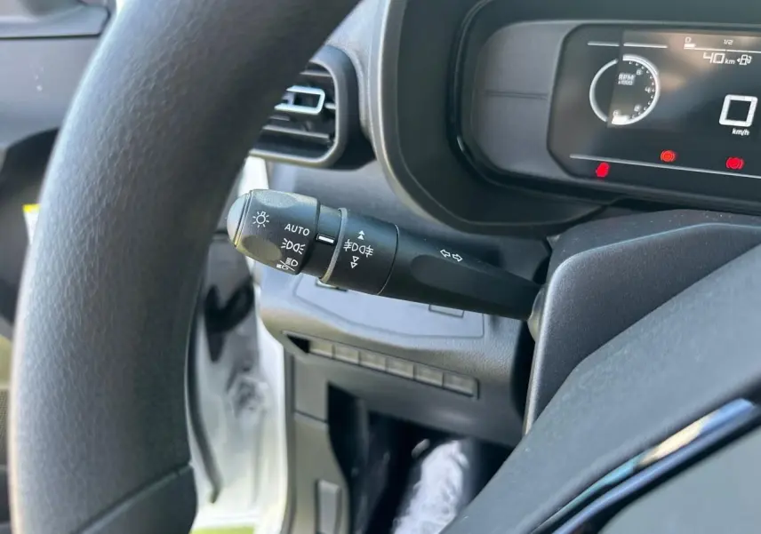 Gros plan sur la manette de commandes d’éclairage à gauche du volant d’un Citroën Berlingo blanc, tableau de bord numérique visible.