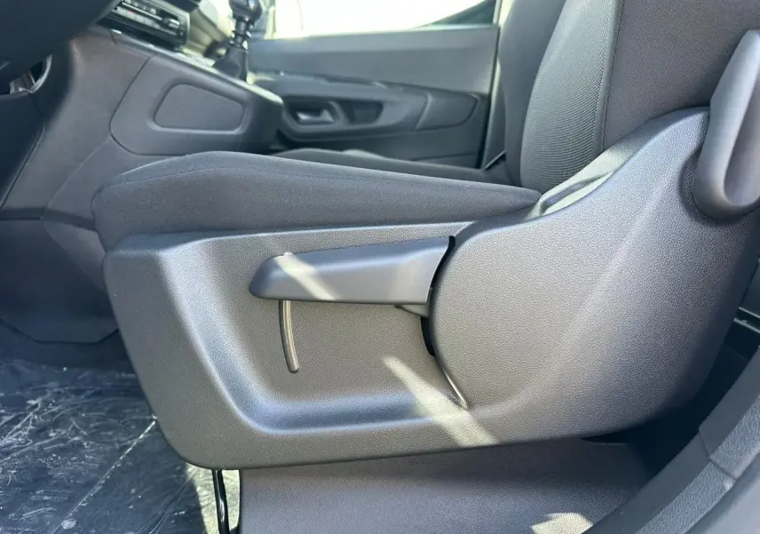 Gros plan sur le réglage manuel du siège conducteur en tissu noir dans l'habitacle du Citroën Berlingo blanc Icy.