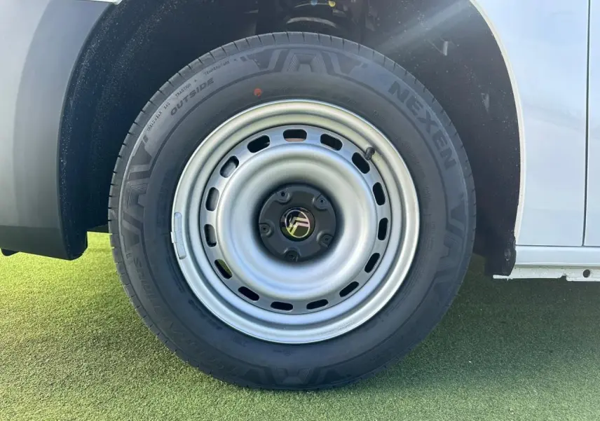 Gros plan sur la roue arrière droite en jante tôle grise du Citroën Berlingo blanc Icy, partie basse de la carrosserie visible.