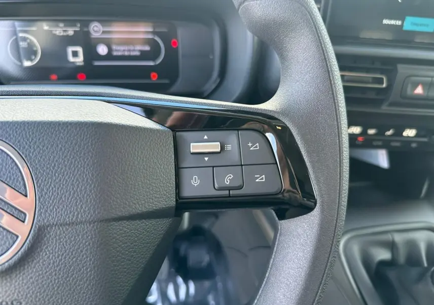 Gros plan sur les commandes du volant noir du Citroën Berlingo blanc Icy, avec tableau de bord numérique en arrière-plan.