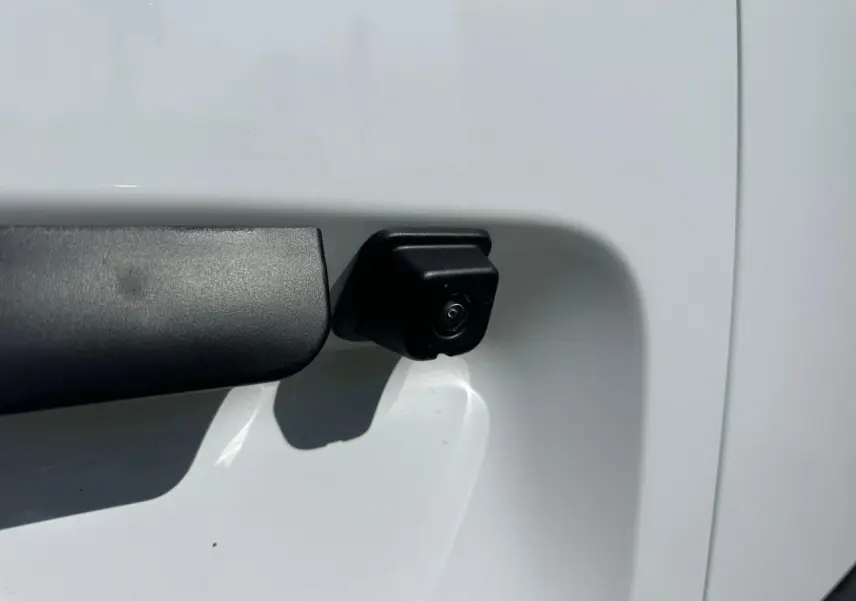 Gros plan sur la caméra de recul noire intégrée à la porte latérale droite du Citroën Berlingo blanc Icy.