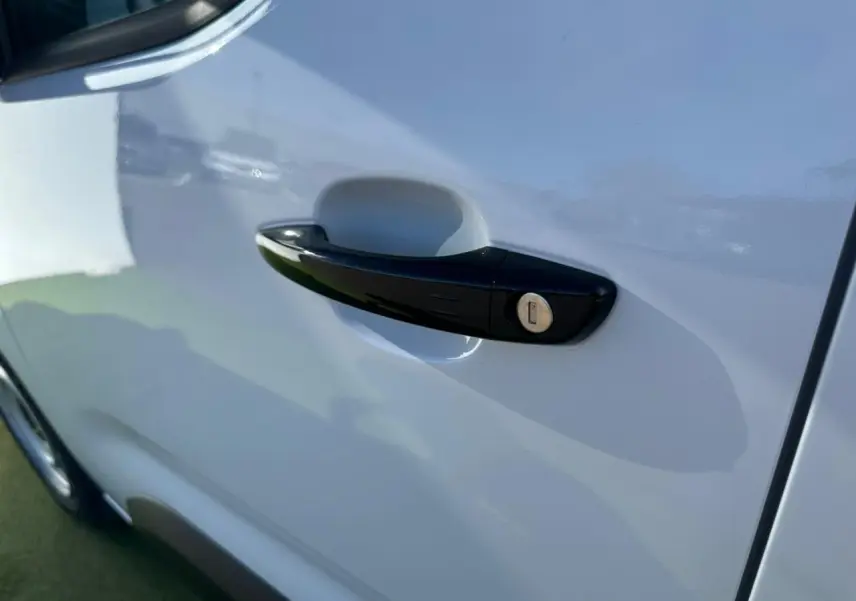 Poignée de porte noire brillante sur la porte avant gauche du Citroën Berlingo III blanc Icy, vue rapprochée en extérieur.