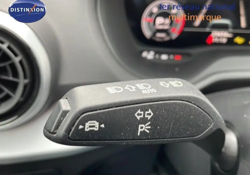 Gros plan sur la commande de clignotant et feux d’un Audi Q2 noir mito metal, intérieur avec tableau de bord flou en arrière-plan.