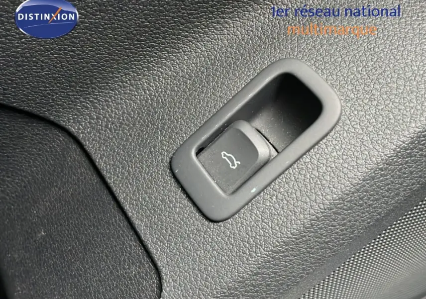 Bouton d'ouverture du coffre sur panneau intérieur noir texturé d'un Audi Q2 noir mito metal, vue rapprochée.