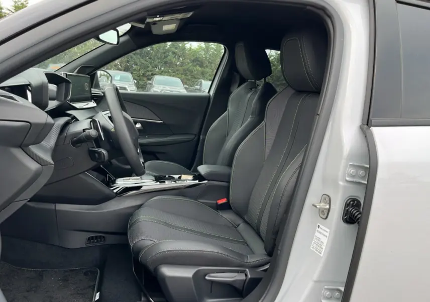 Vue intérieure côté conducteur du Peugeot 2008 Hybrid 145 GT Vision blanc okénite, sièges cuir tissu noirs avec surpiqûres vertes.