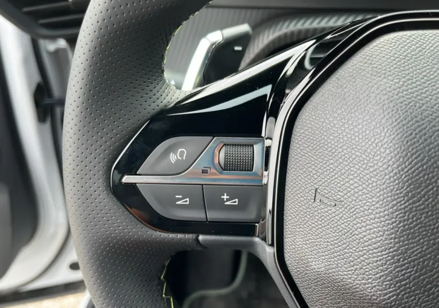 Gros plan sur le côté gauche du volant cuir perforé de la Peugeot 2008 Hybrid 145 avec commandes multifonctions.