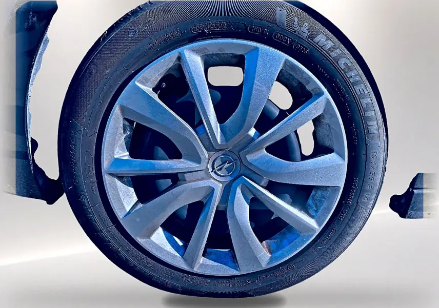 Gros plan sur la roue avant gauche de l’Opel Corsa noire, mettant en valeur la jante alu et le logo Opel central.