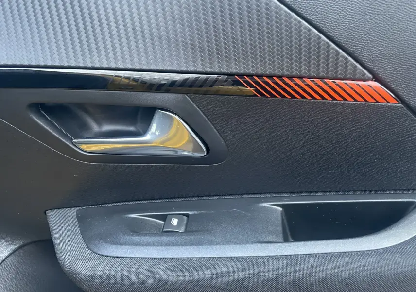 Détail de la poignée intérieure côté gauche de la porte d'une Peugeot 208 électrique jaune 2023 avec insert décoratif rouge.