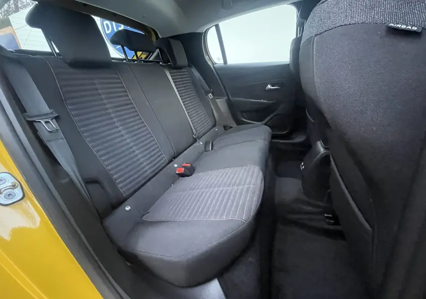 Vue intérieure arrière côté gauche de la Peugeot 208 électrique jaune 2023, montrant les sièges arrière noirs en tissu.