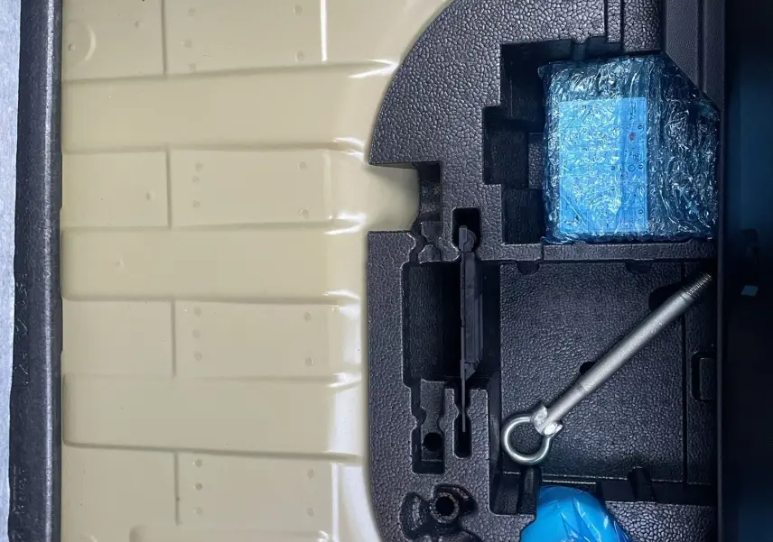 Coffre ouvert d'une Peugeot 208 électrique jaune 2023, montrant le rangement sous plancher avec outils et accessoires emballés.