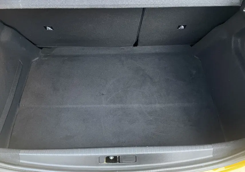 Coffre ouvert vu de dessus d'une Peugeot 208 II électrique jaune 2023, montrant un espace de rangement vide et propre.