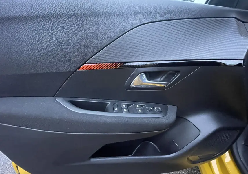 Détail de la porte avant gauche de la Peugeot 208 électrique jaune 2023, avec commandes de vitres et insert décoratif rouge.