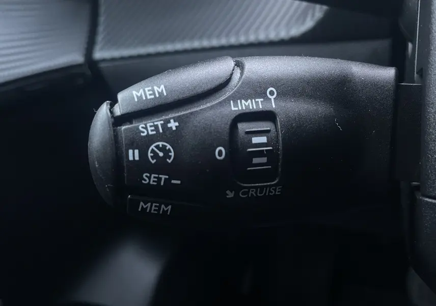 Gros plan sur la commande de régulateur de vitesse noire dans l'habitacle d'une Peugeot 208 électrique jaune 2023.