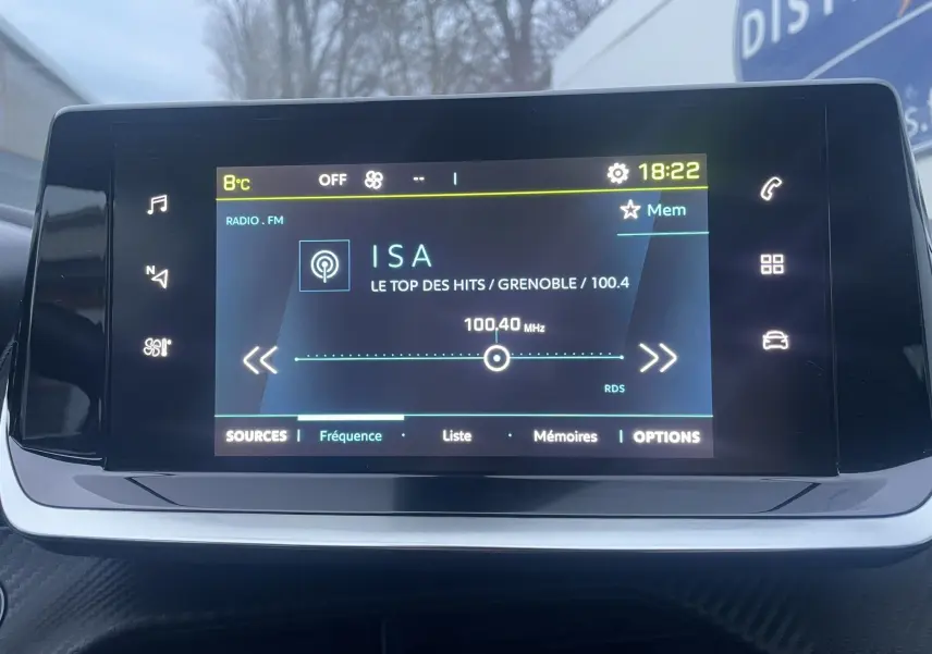 Écran tactile central du tableau de bord de la Peugeot 208 électrique 2023 affichant la radio FM sur fréquence 100,4 MHz.