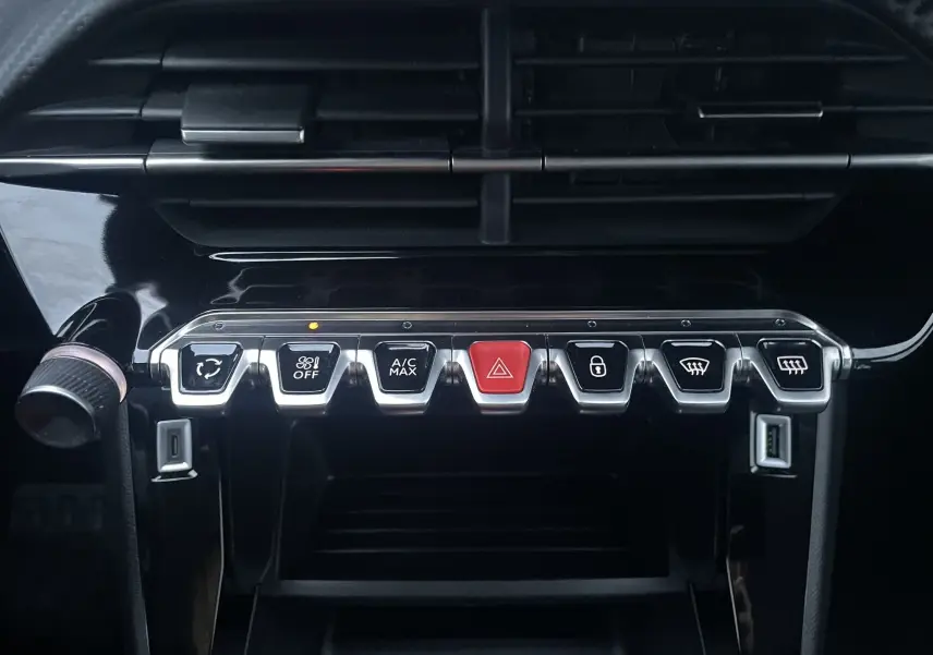 Gros plan sur les commandes centrales noires et chromées du tableau de bord du Peugeot 208 II électrique jaune 2023.